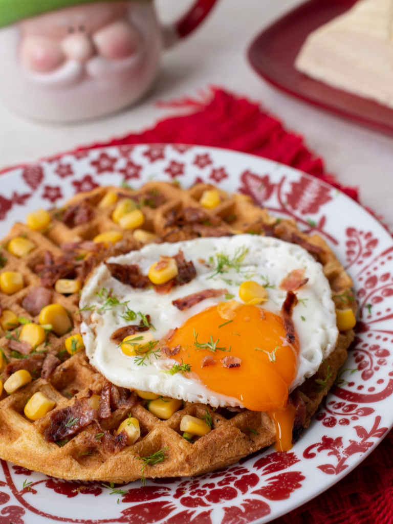 Foto en primer plano de waffles de buñuelo servidos con un huevo, maíz y tocineta.