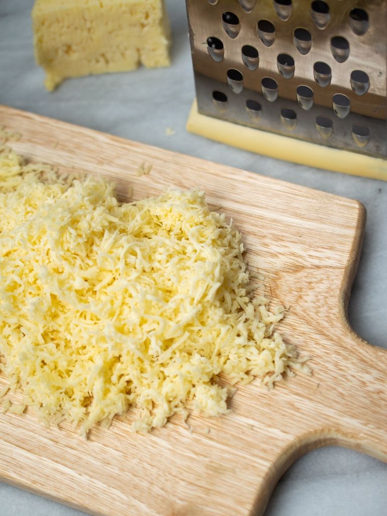 Para añadir a la masa del bollo limpio, queso blanco rallado sobre una tabla de picar de madera.